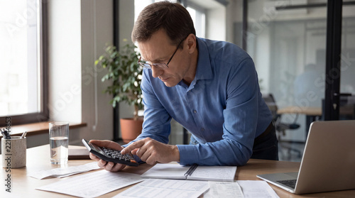 Mature businessman using calculator at office desk with paperwork