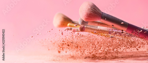 Make up brushes with powder splashes isolated on pink background