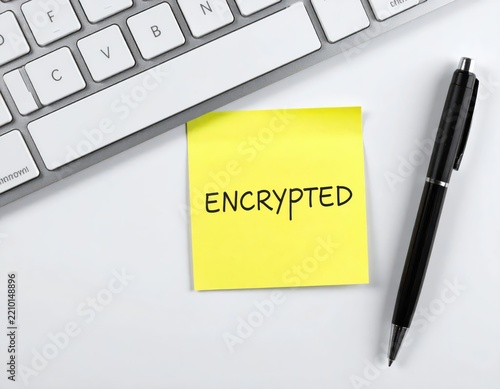 Bright yellow sticky note with the word encrypted placed on a white desk beside a keyboard and pen