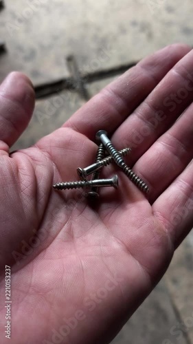 A close-up shot of a hand holding several silver-colored self-tapping metal screws in an open palm.