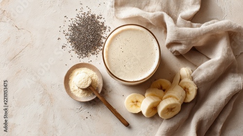 Healthy banana chia seed smoothie ingredients with protein powder and milk. Glass of creamy smoothie sits next to sliced bananas, chia seeds, protein powder, ready to be blended for nutritious drink