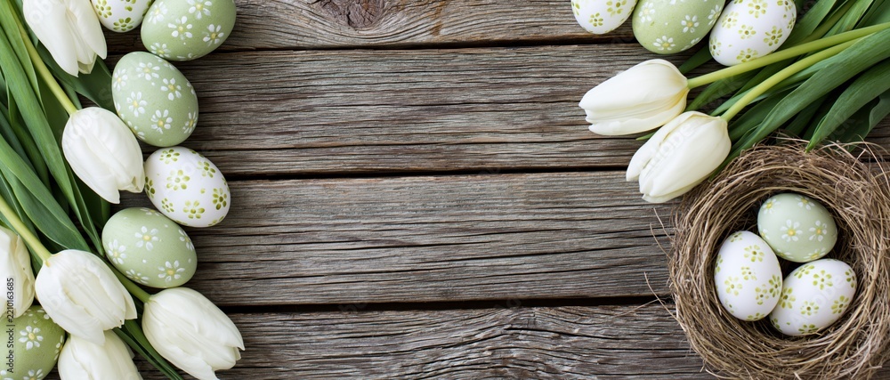 Obraz premium White tulips and painted eggs arranged around a wooden table with a nest in the corner