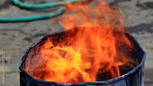 A large flame burns inside a black metal drum on a paved surface, illustrating fire hazards, emergency preparedness, safety awareness, and outdoor fire prevention practices in Indonesia today now.