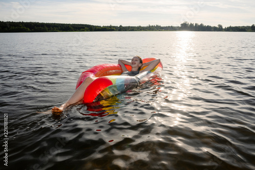 A smiling girl floats on an inflatable mattress in a sunny lake