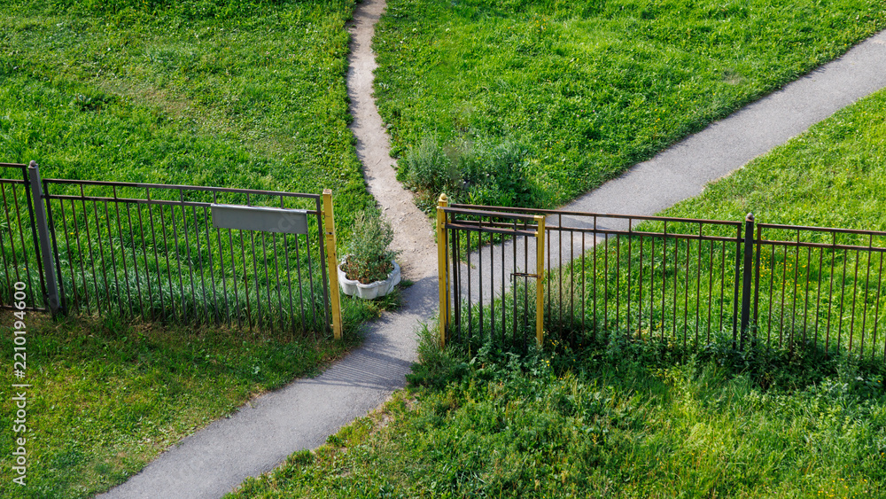 Obraz premium Grassy path splits at wooden gate with metal fencing