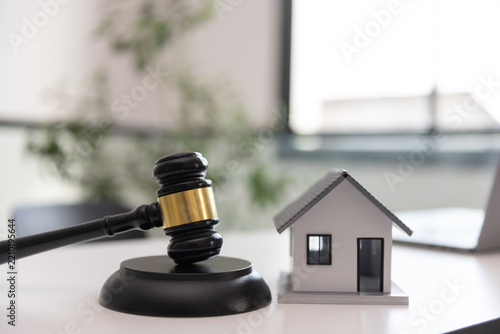 Wooden judge gavel next to a model house in a modern office, symbolizing property law, home ownership, real estate disputes, housing contracts, mortgage issues, and legal protection.