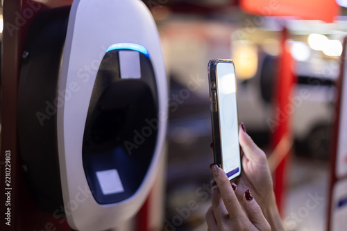 Close-up shot of a woman's hand using a smartphone to scan and pay for electric vehicle charging at a charging station