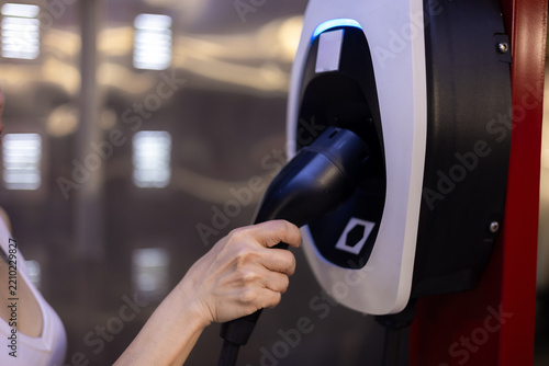 Woman is putting the charging connector back into the charging station after finishing charging her car