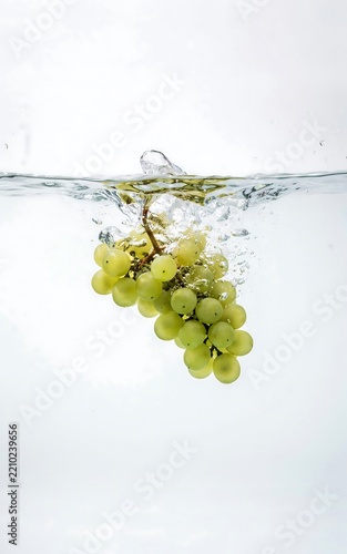 Bunch of fresh green grapes submerged in clear water creating bubbles and splashes on white