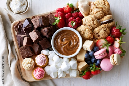 Dessert grazing board cookies brownies strawberries macarons and caramel sauce for party platter background and entertaining display
