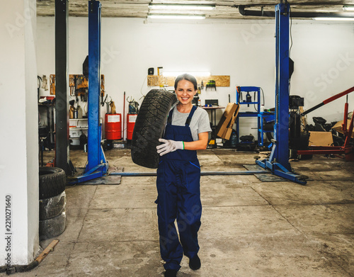 Female mechanic carrying a car wheel on her shoulder in automotive service station