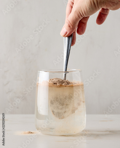 Close up of protein powder added and stirred with spoon in glass