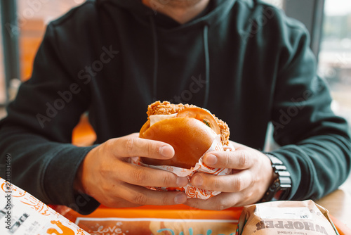 Close-up portrait of a young caucasian man holding a large delicious hamburger or cheeseburger, getting ready to take a bite in a modern restaurant interior. 