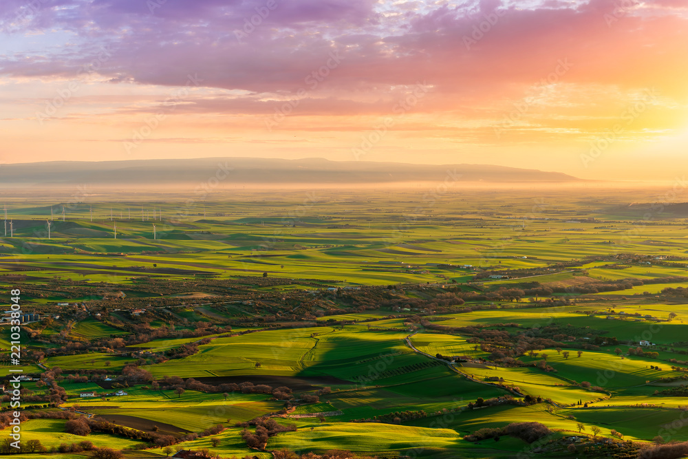 Fototapeta premium beautiful panoramic landscape of green valley fielis and hills during spring sunet or sunrise with agricultural farms and colorful cloudy sunset on background