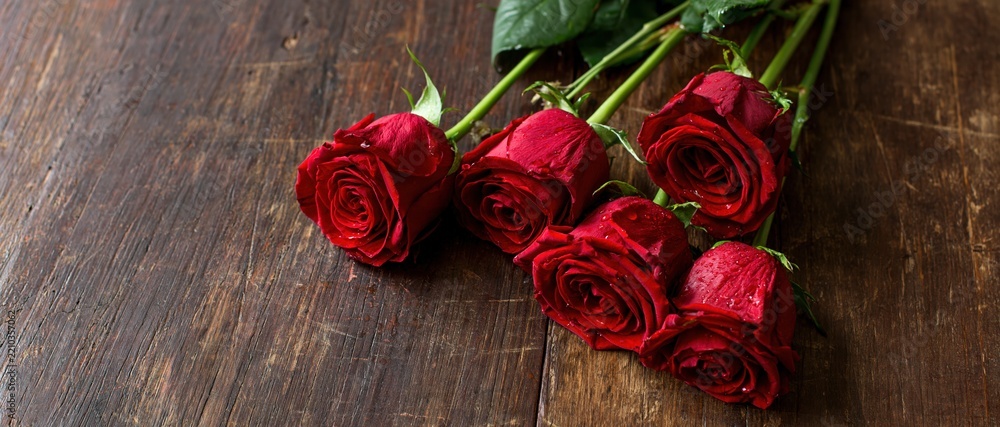 Naklejka premium Five red roses with water droplets arranged on a dark wooden table