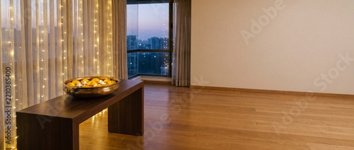 Brass bowl with floating candles and marigold flowers placed on wooden bench in modern room with flowers sits minimalist decorated string lights lights near large celebration traditional interior