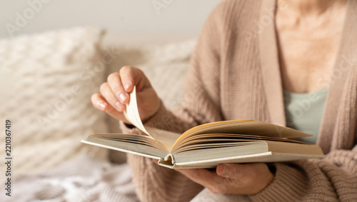 Woman reads book, turns page, and enjoys her leisure time indoors. Cozy moment of reading and self-education. Concept of slow and mindful living