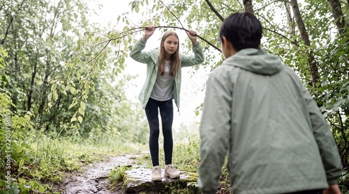 Teenage girl lifts a wet branch on a forest hiking trail