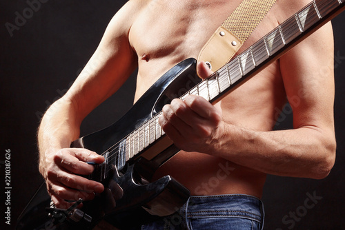 Rock musician playing solo on electric guitar on dark stage.