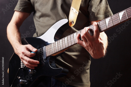 Posing hands of musician playing the black guitar on dark stage.