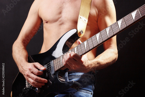 Hands of artist with black guitar on dark stage.
