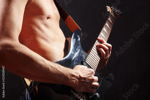 Artist playing solo on black guitar on dark stage.