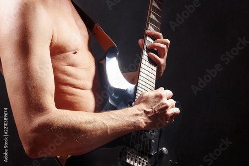 Rock musician playing solo on black guitar on dark stage.