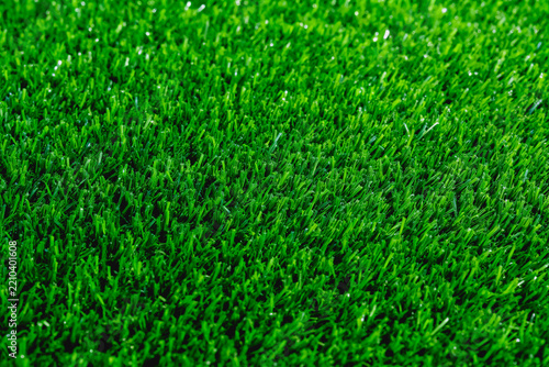 A close-up shot of dense, vibrant artificial green turf, showing fine synthetic grass blades and uniform texture. Suitable for use as a background or surface material.