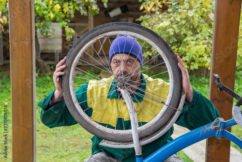 A 50-year-old European man is repairing a bicycle on the porch of his house.