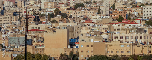 View of the dense urban landscape of Jerash featuring residential buildings, rooftops with water tanks, and a street lamp in the foreground in Jerash, Jerash Governorate, Jordan.