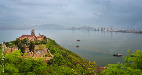 View from Phuoc Mai Lighthouse to Quy Nhon city with fishing boats in foreground, Vietnam. Scenic coastal view from Hai Minh peninsula with lighthouse, sea, mountains, and cityscape.