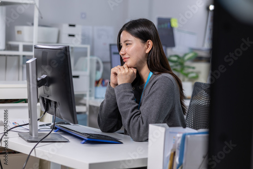 Asian woman working at computer in modern office, focused and thoughtful during quiet workday