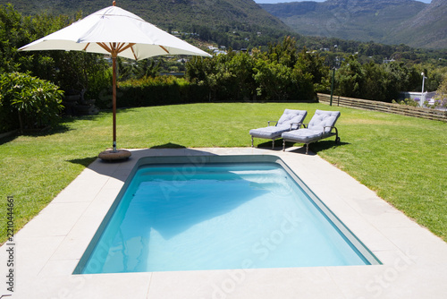 Rectangular in-ground swimming pool is sparkling on tiled deck under large white umbrella shadow