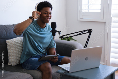 African American man sitting in studio wearing teal tee, white phones talking to mic, copy space