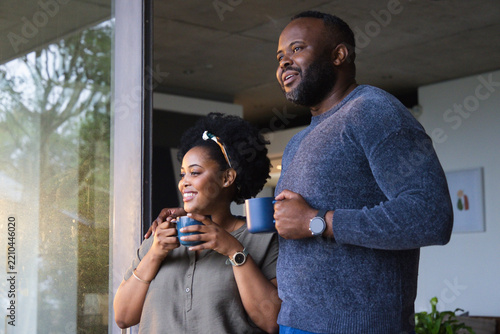 African couple standing at home near glass door holding blue ceramic mugs wearing headband