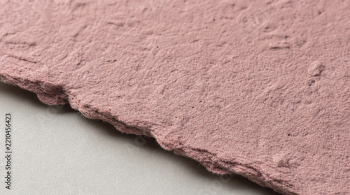 Macro photograph of single thick sheet of molded recycled paper pulp with rough pink texture and torn edge, showing sustainable material detail and natural fiber surface