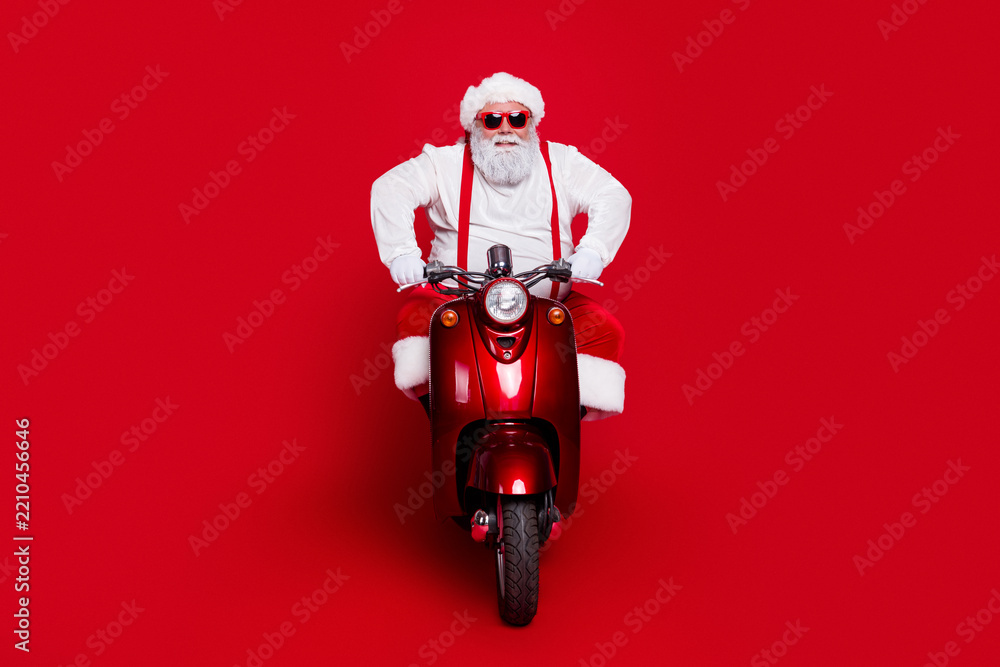 Obraz premium Santa Claus riding a red scooter wearing sunglasses and festive outfit against a bold red background, playful Christmas portrait conveying fun, holiday spirit and modern seasonal style