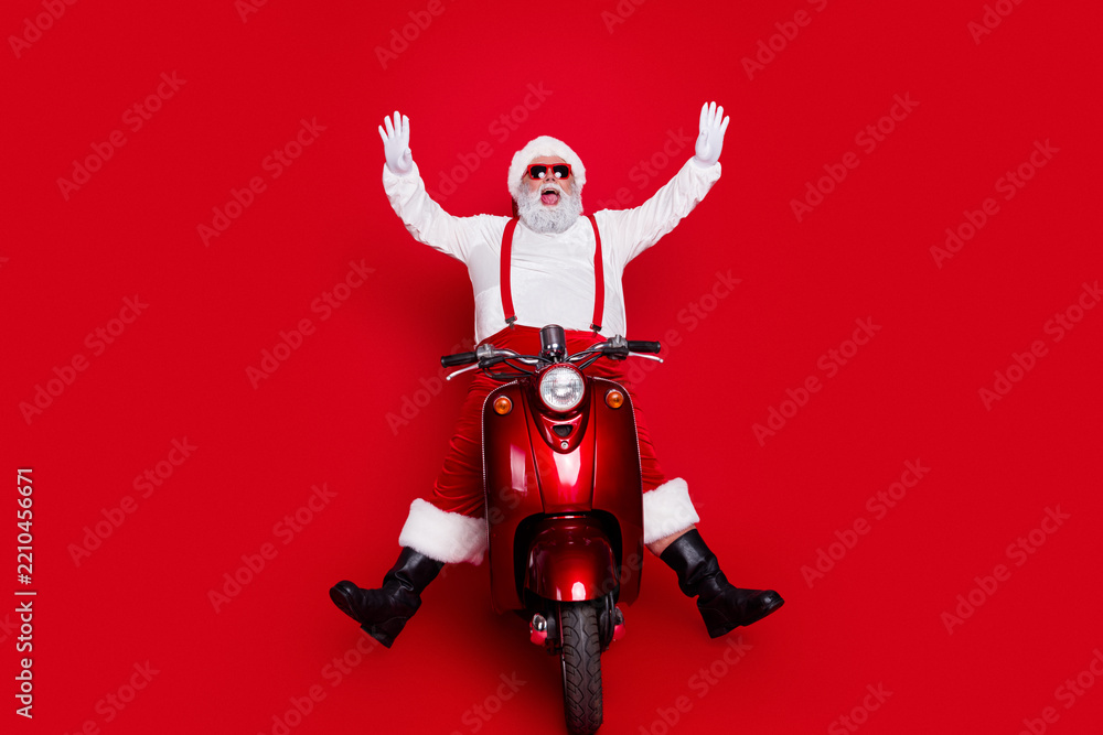 Obraz premium Santa Claus riding a red vintage scooter with arms raised, wearing sunglasses and white gloves celebrating Christmas and holiday fun against a bright red background