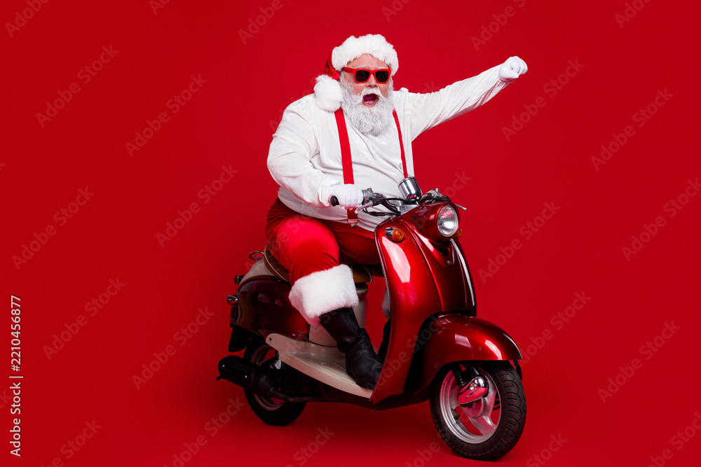 Obraz premium Santa Claus riding a red scooter with sunglasses and raised fist, a festive Christmas character delivering playful holiday cheer against a bold red background