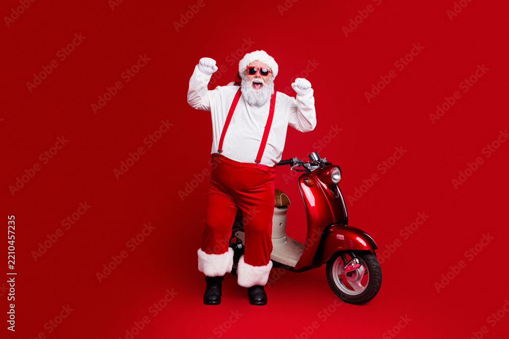Obraz premium Santa Claus in red sunglasses cheering beside a vintage red scooter on a bold red background for playful Christmas holiday celebration