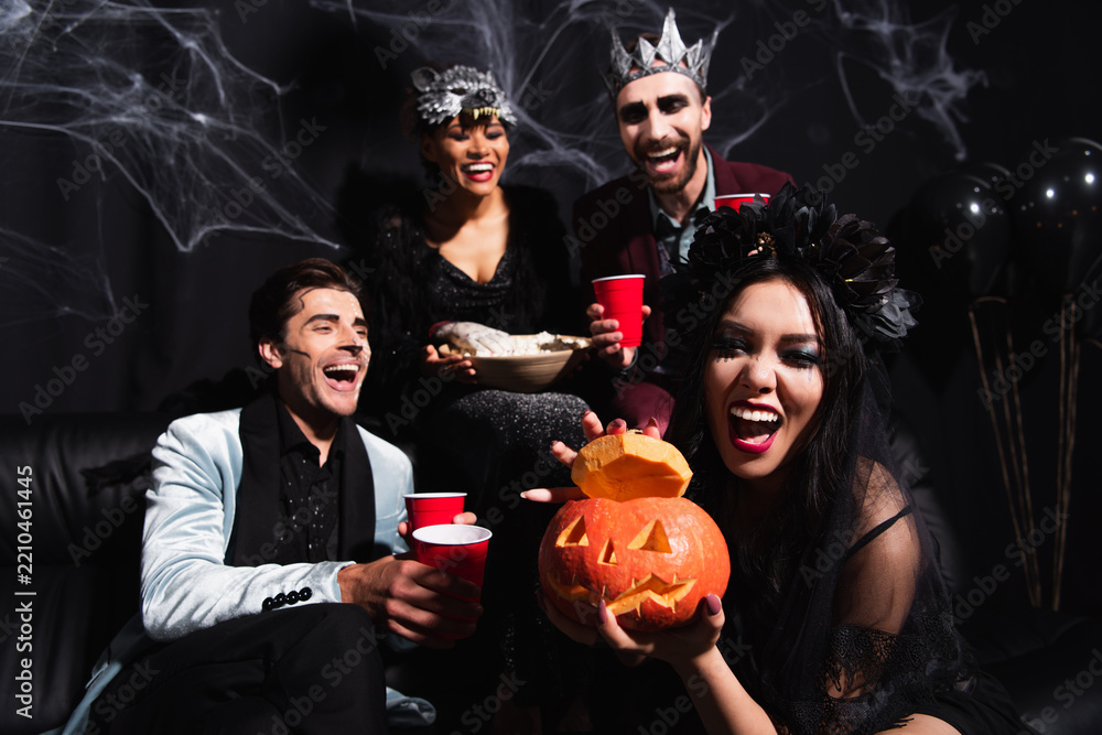 Obraz premium Celebrating Halloween with asian woman holding carved pumpkin near multicultural friends in costumes