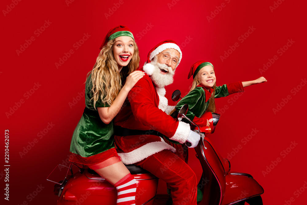 Obraz premium Santa Claus with two cheerful elves riding a red scooter celebrating Christmas joy and holiday family fun