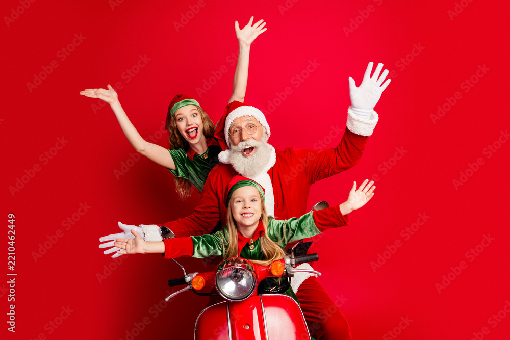 Obraz premium Santa and two cheerful elves riding a red scooter in a family Christmas celebration full of joy, holiday fun, festive costumes and playful seasonal spirit