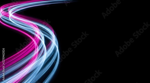 Abstract multicolored neon pink and light blue light trails flowing in a dynamic wave pattern on a black background with copy space