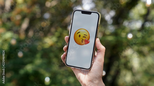 hand holding a cellphone with an emoji sending a kiss and a smile, online communication, emotions, love, support