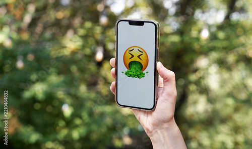 Fotografie hand holding a smartphone with a vomiting smiley face, isolated, concept of disg