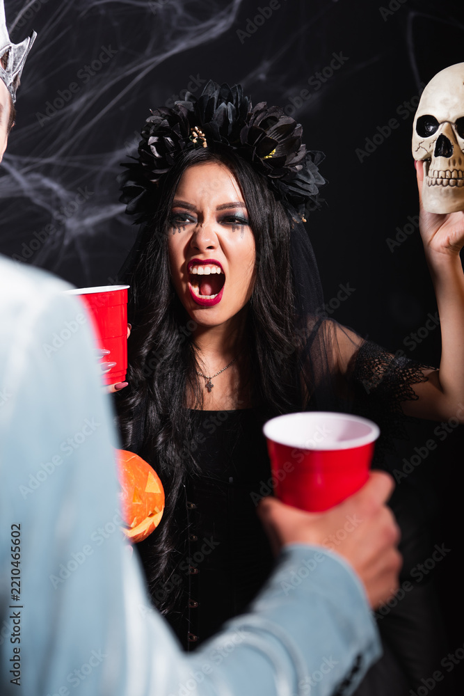 Obraz premium Young asian woman scaring her friend with skull while celebrate Halloween in creative costume