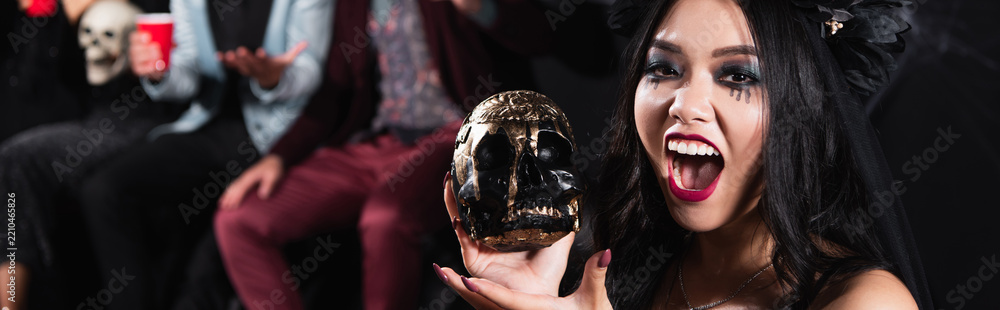 Obraz premium Excited asian woman celebrates Halloween with creepy skull, banner 
