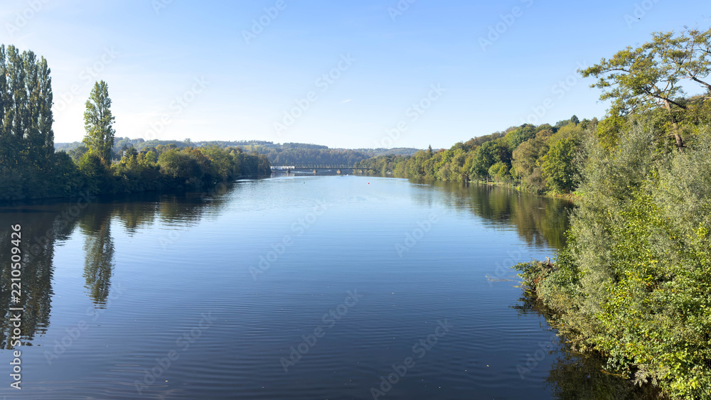 Obraz premium Wide landscape view across the Ruhr valley with calm water, woodland and a distant railway bridge.