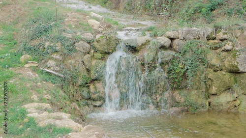 Small Natural Waterfall Cascading Over Rustic Stone Wall in Serene Rural Landscape